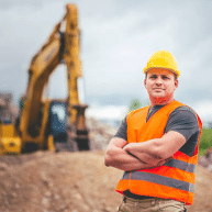 Ouvrier sur chantier devant une pelle mécanique.